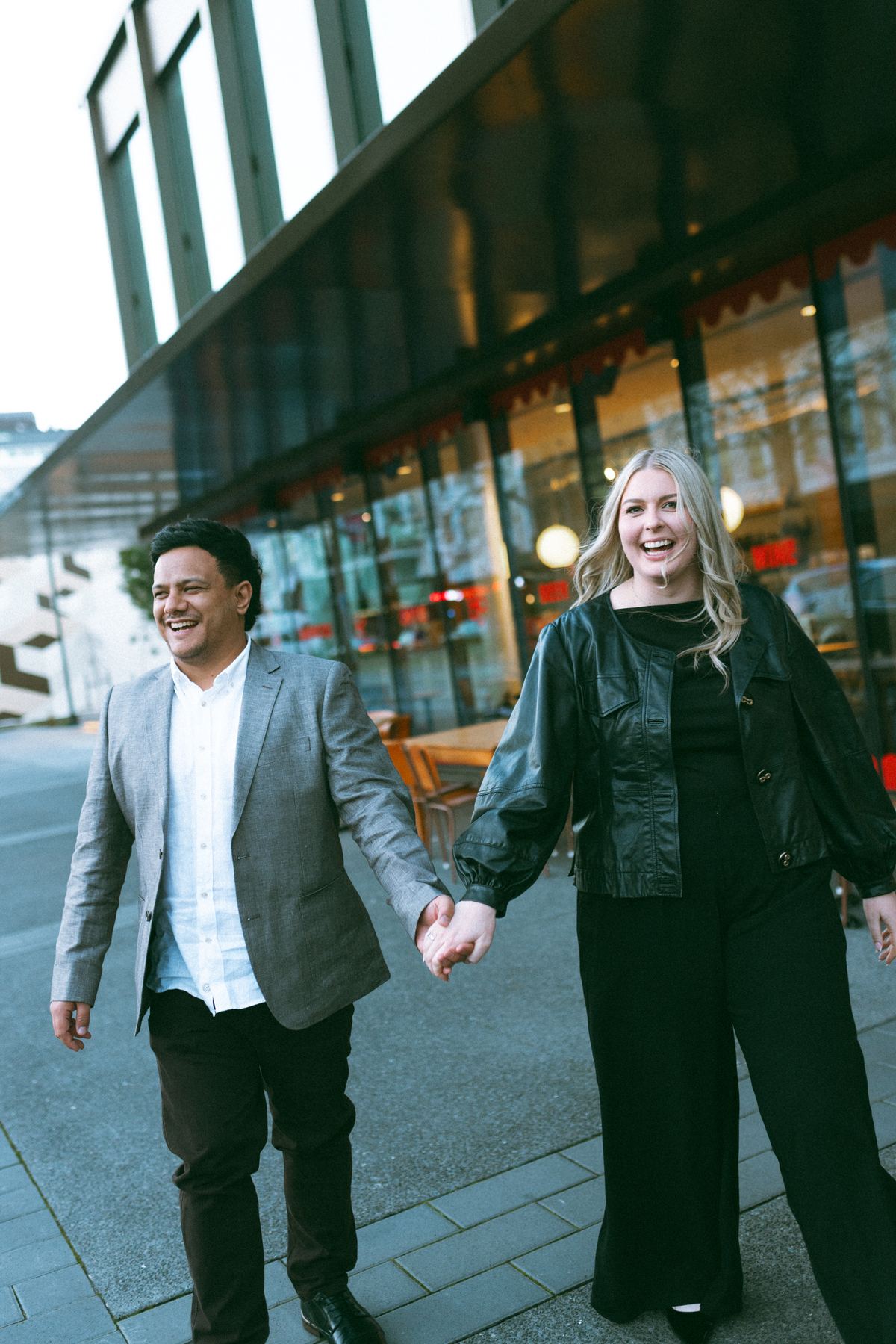 Zoe and Tyler laughing as they walk hand in hand along a city street