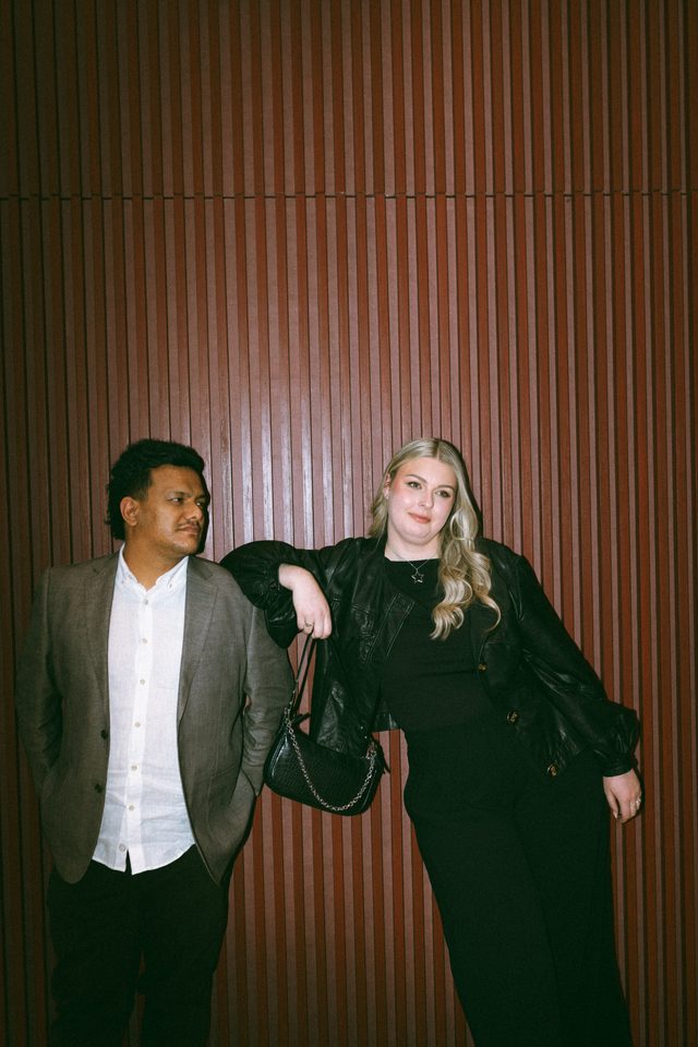 Zoe leaning on Tyler's shoulder against a timber wall