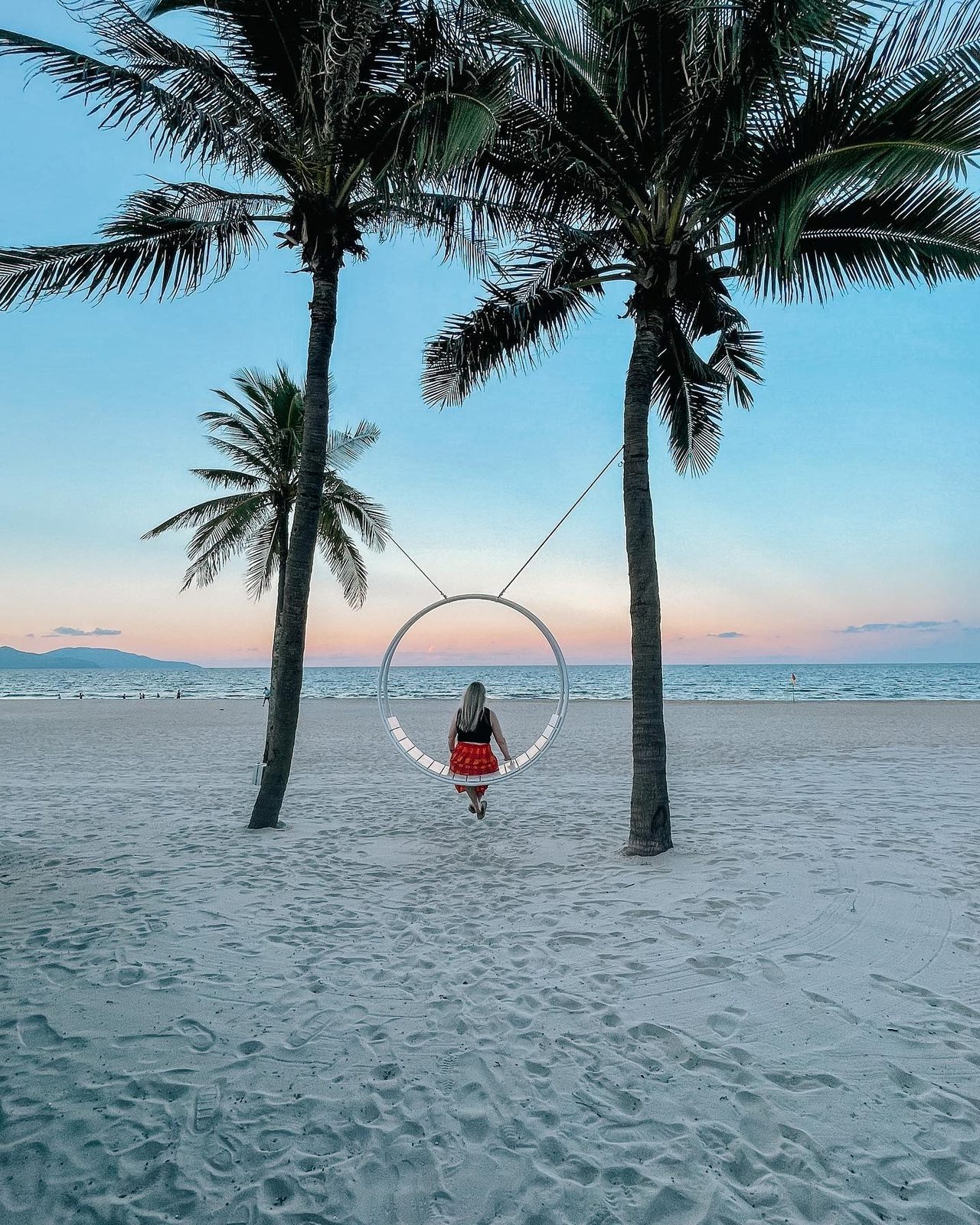 Zoe on a ring swing between palm trees on the beach in Da Nang at sunset